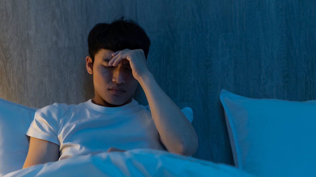 Tired and frustrated man lying in bed along wearing a white t-shirt