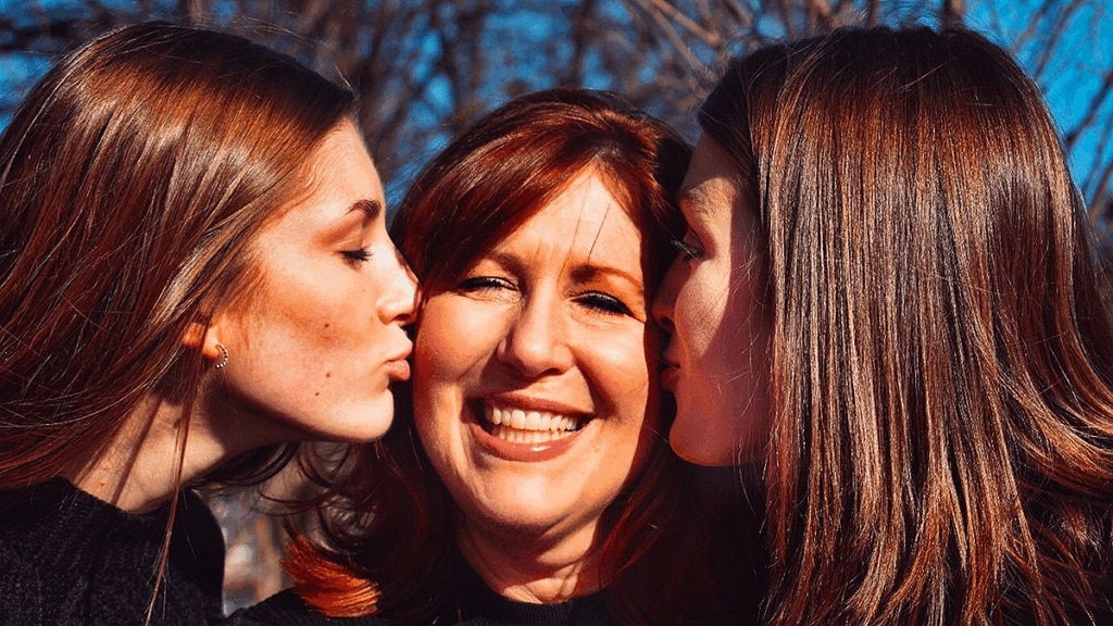 Two daughters kissing mother