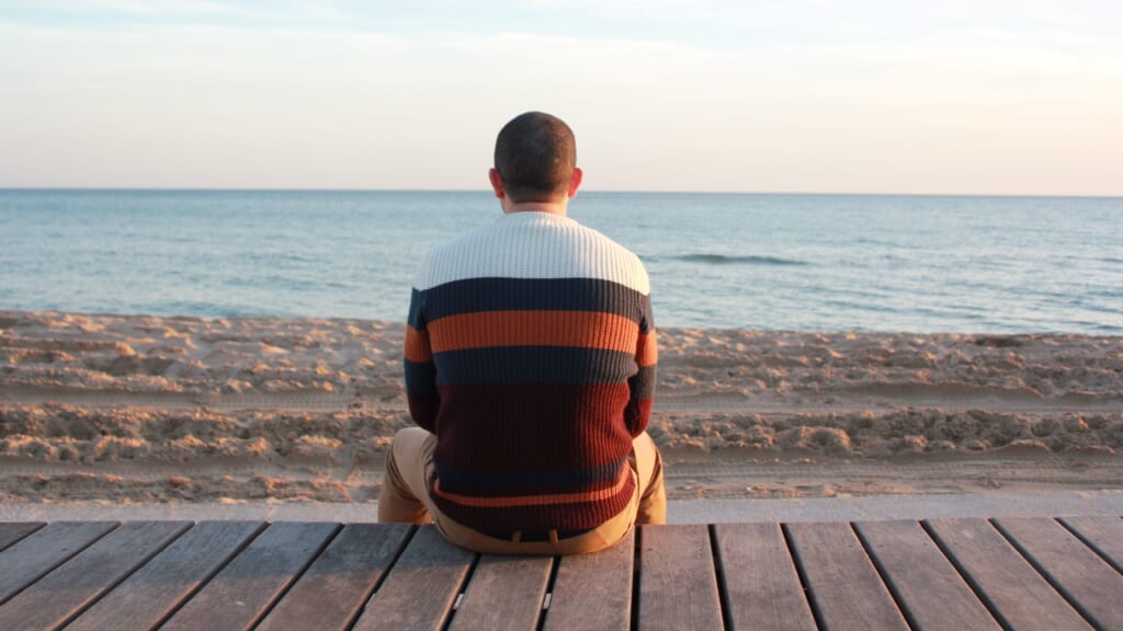 Man sitting alone on wooden panel facing the ocean
