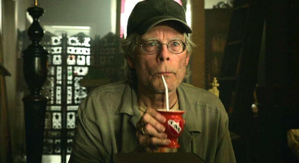 Stephen King in cap drinking out of a straw.